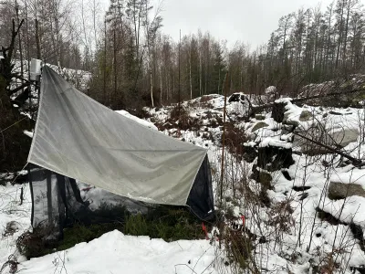 A translucent white cloth tent stretched between bare trees in a snowy forest landscape