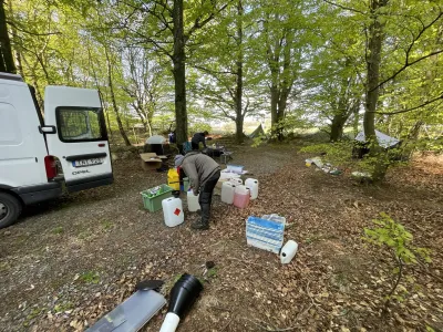People organizing supplies and equipment in a forest clearing next to a white van